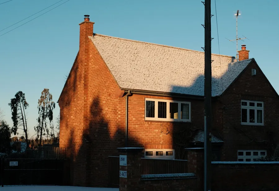 Red brick house with a frosted tiled roof, gable, ridge and chimney in low winter sun