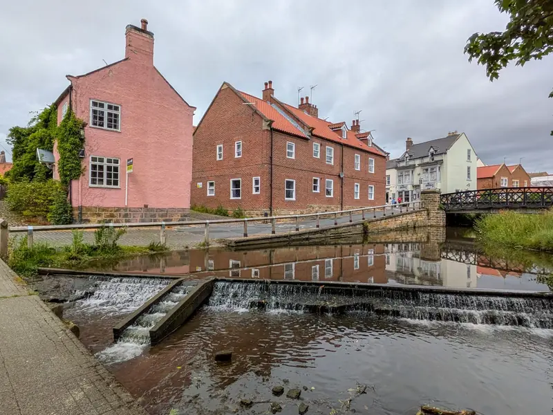 Brick houses beside a swollen stream under a grey sky the morning after a storm, when Mansfield homeowners should check the roof and loft