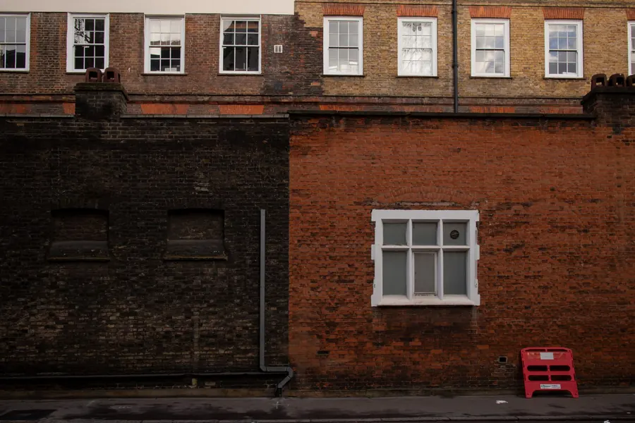 Red and dark brick walls with a downpipe and long dark staining patterns, the kind of marks a failing gutter leaves on Mansfield brickwork