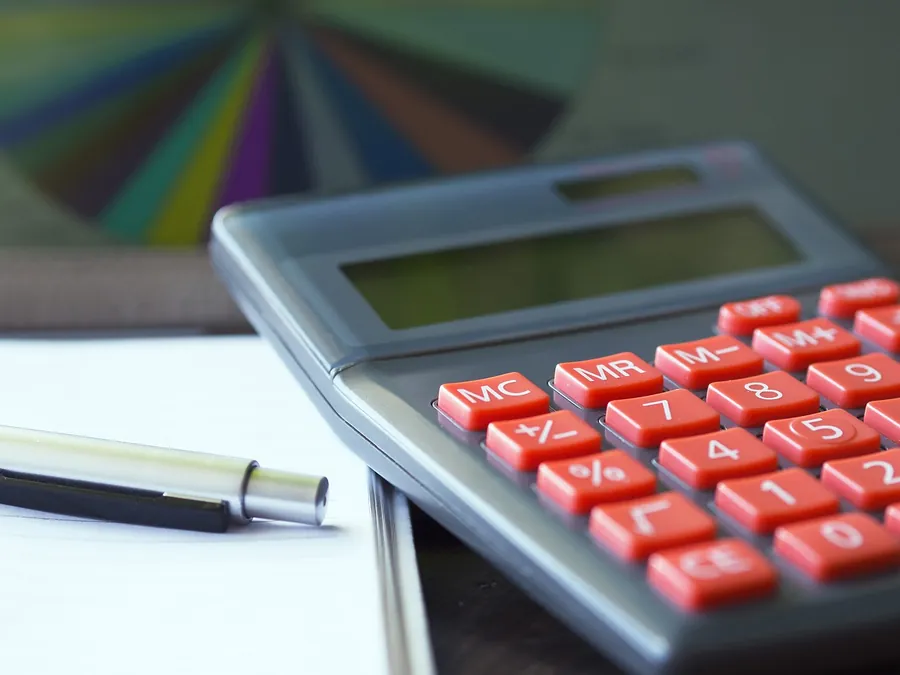 Grey calculator with red keys lying beside a pen on a sheet of paper