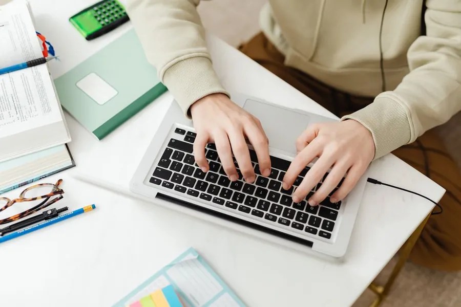 Hands typing on a laptop keyboard at a desk while researching a company online