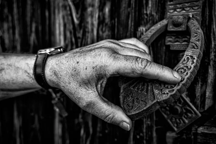 Close up of a hand reaching for a heavy metal knocker on a wooden front door