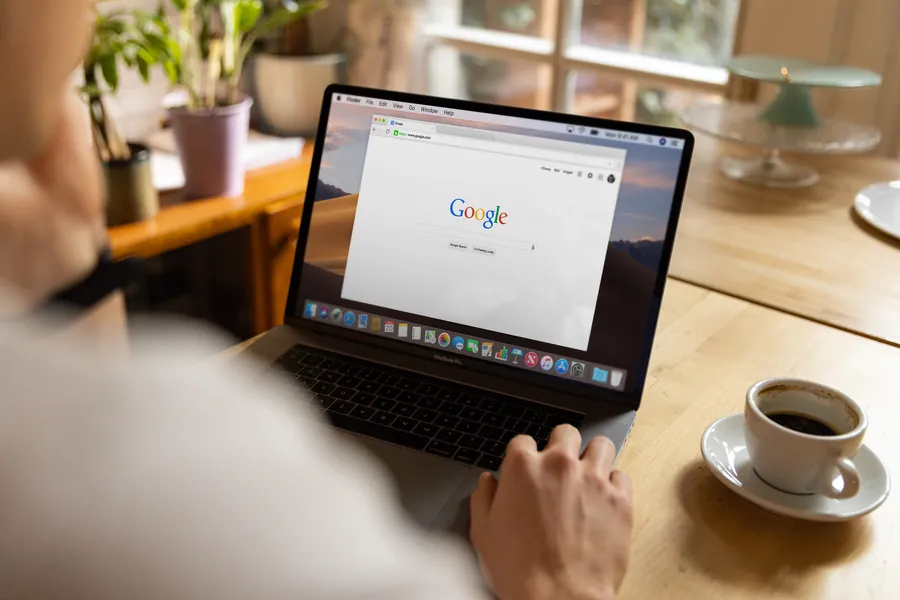 Homeowner at a wooden table searching a roofing company name on a laptop