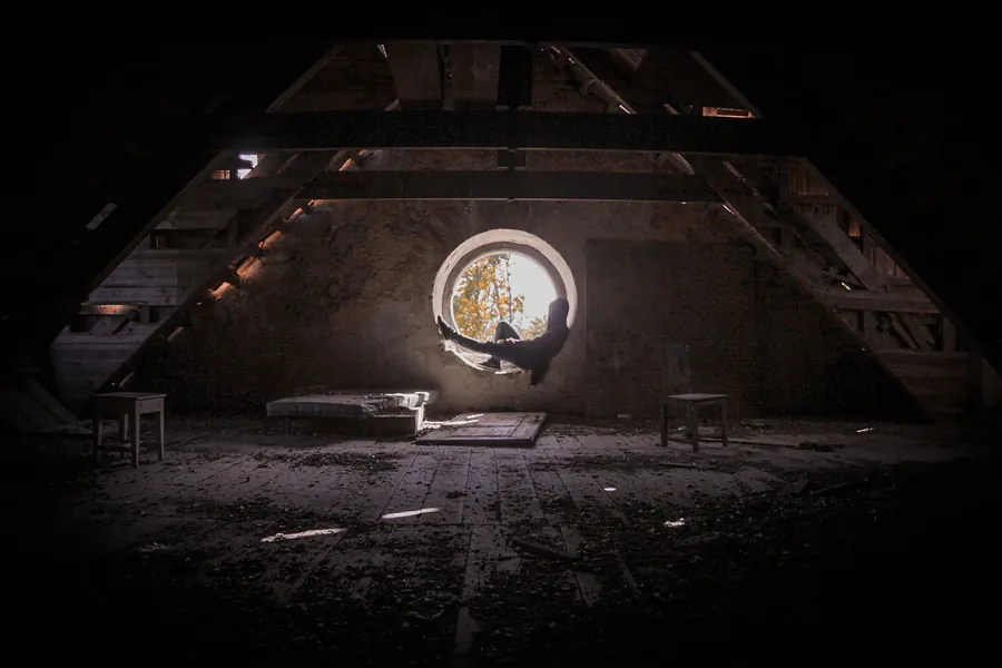 Dim loft space with roof timbers lit through a small window, the kind of view a torch gives during a check