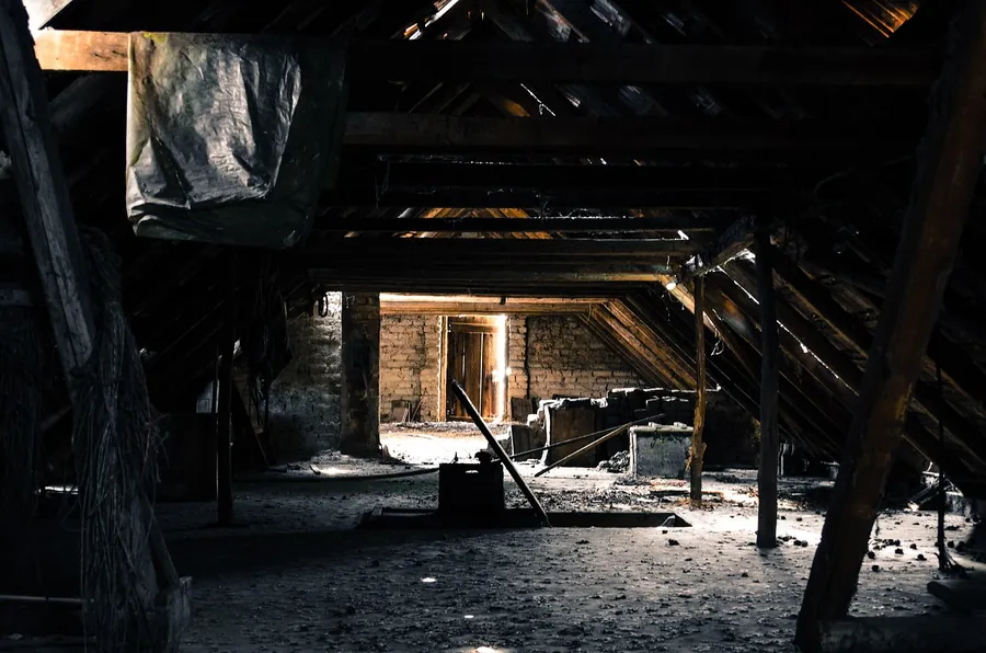 Dark old attic with timber rafters and small chinks of daylight showing through gaps in the roof covering
