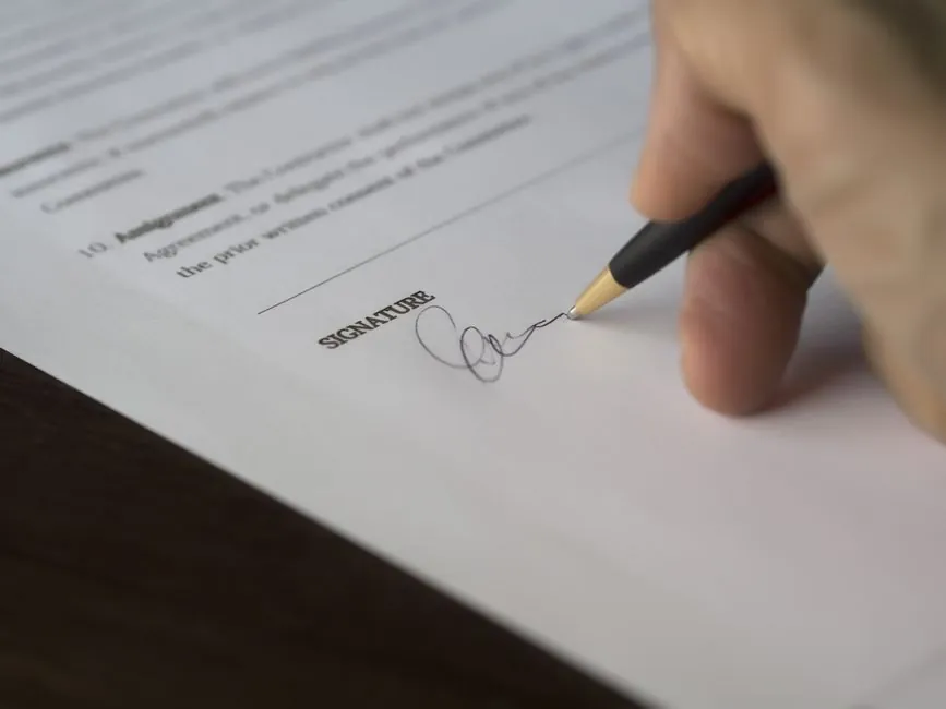 Hand signing a printed contract above the signature line with a pen