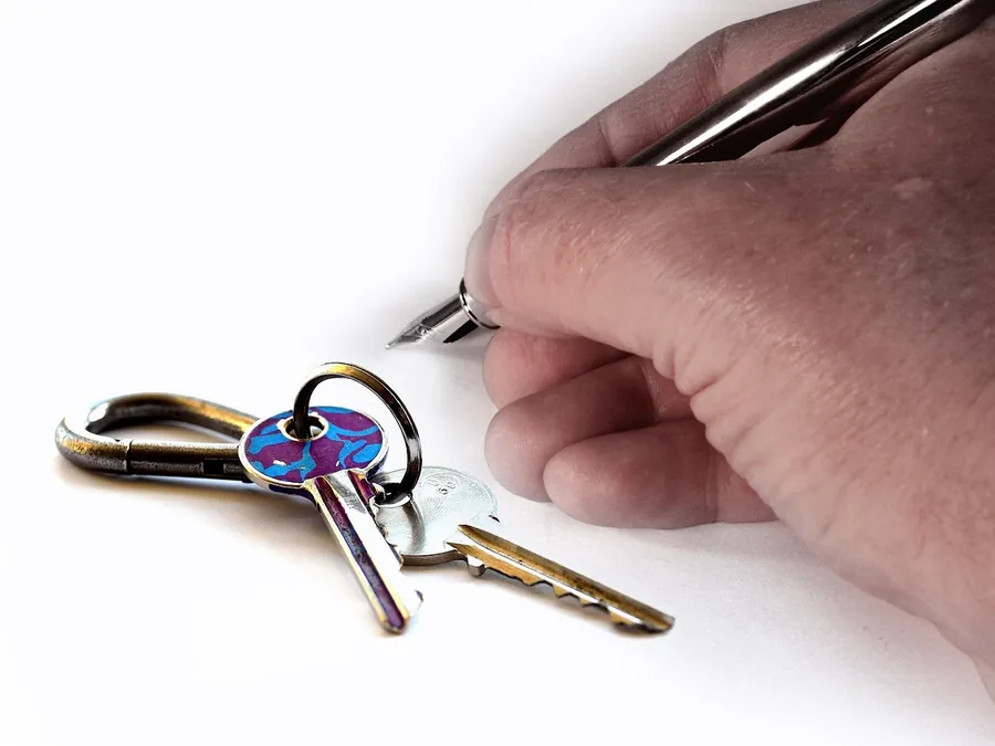 Hand signing a document with a fountain pen beside a set of house keys