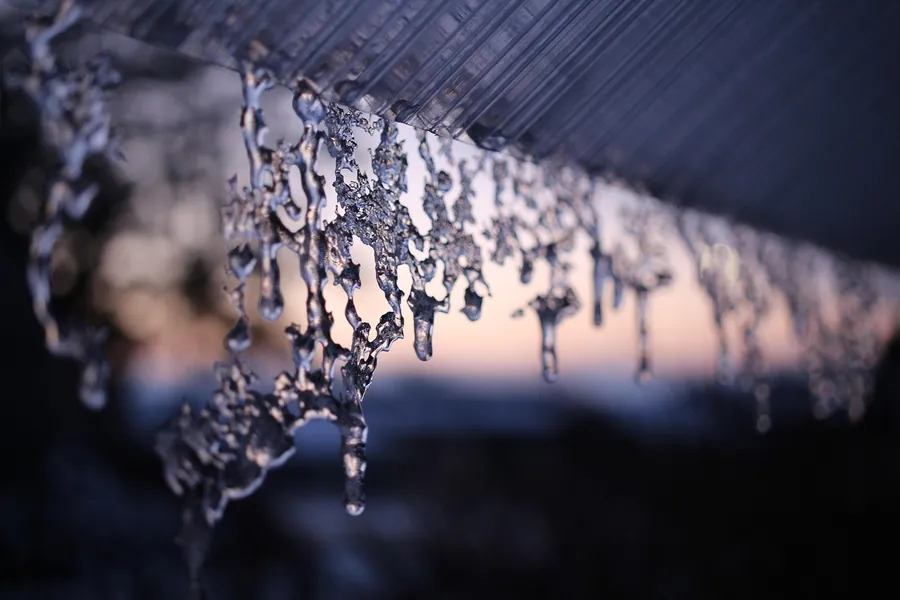 Row of icicles hanging from a frozen roof edge against a dusky winter sky