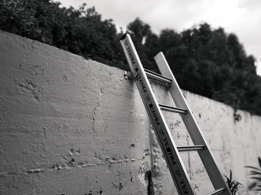 Aluminium ladder secured against a rendered wall, the first stage of reaching the roofline for a gutter and fascia job in Mansfield