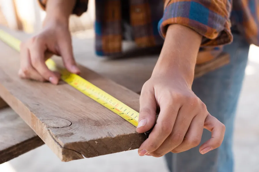 Hands measuring a length of timber with a yellow tape measure