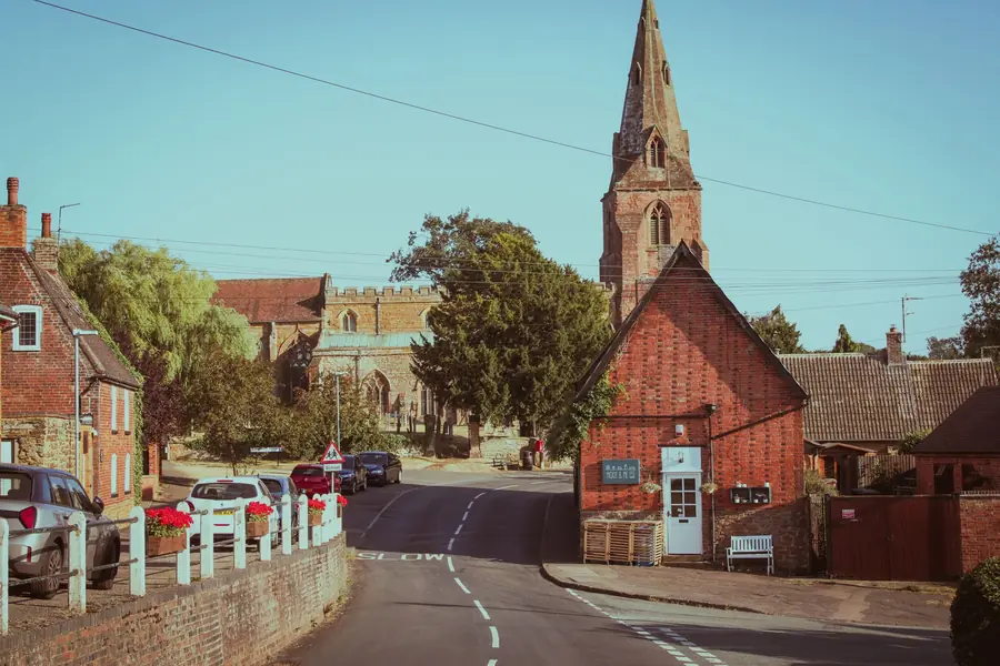 Red brick village street in Nottinghamshire with parked cars and a church spire