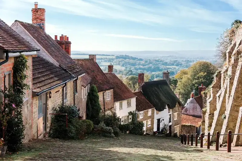 Steep street of old English village houses with tiled roofs and brick chimneys above open countryside