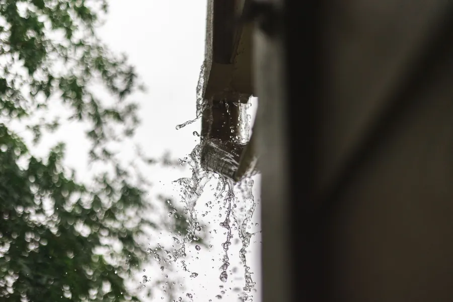 Rainwater pouring off a roof edge in heavy rain, the kind of run-off a missing lead flashing sends inside the house