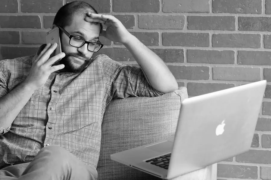 Worried man on a phone call at home with a laptop open in front of him
