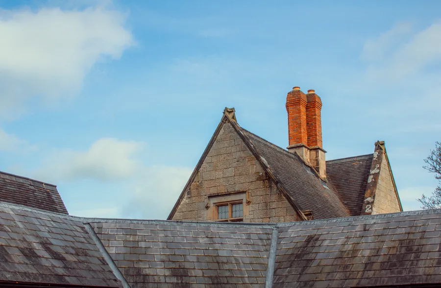 Slate roof slopes and a tall brick chimney seen from below against a blue sky