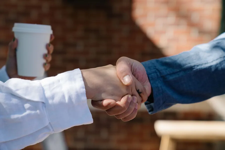 Homeowner and roofer shaking hands beside a brick wall after agreeing the work