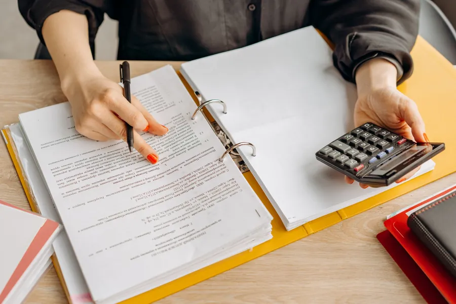 Hands going through a printed quote with a pen and calculator at a desk
