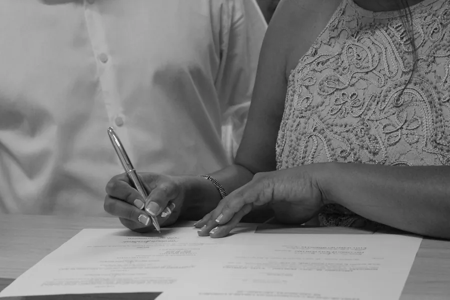 Black and white close up of two people signing a printed document at a table