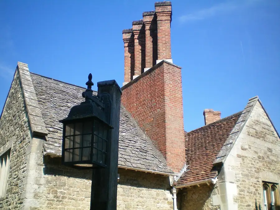 Stone gable and tiled roof with a tall brick chimney stack and pots against a blue sky