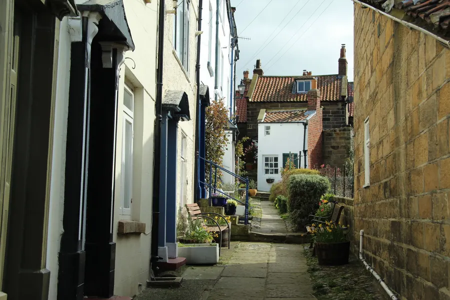 Narrow row of older terraced houses with downpipes and gutters running past several front doors, like the colliery-era rows around Mansfield
