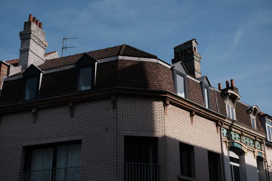 Victorian brick corner building with a slate mansard roof, dormer windows and tall chimney stacks