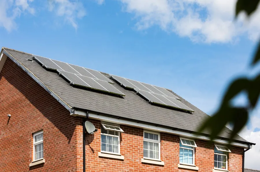 Red brick house with a slate roof and solar panels fitted, the kind of measure funded by home energy grants