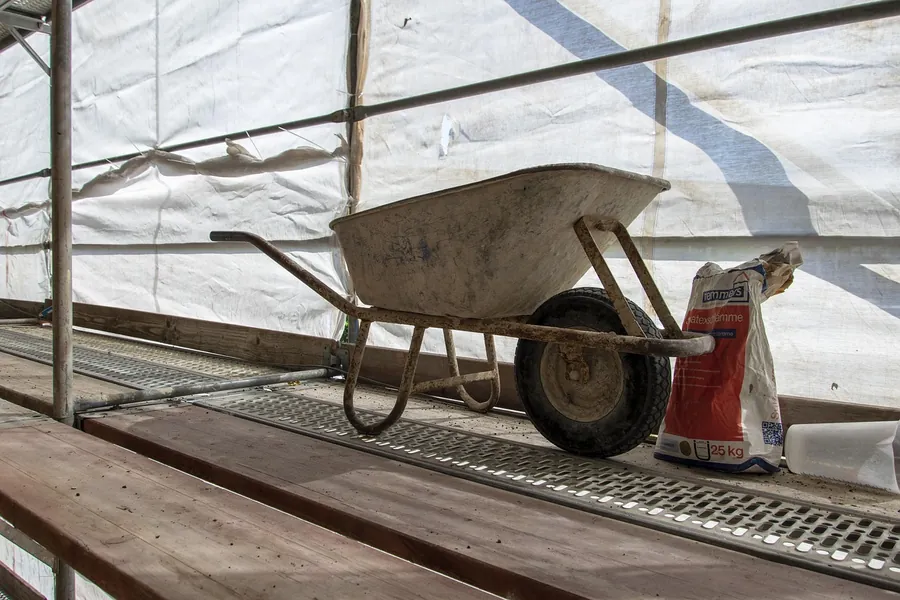 Wheelbarrow and a bag of cement on scaffold boards behind protective sheeting