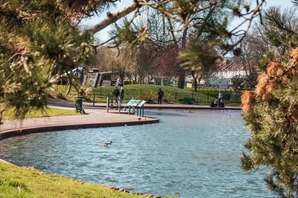 Ornamental lake in a public park with lawns, paths and visitors under mature trees