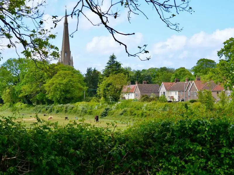 Brick cottages with clay tile roofs beside a field, a church spire behind the trees, an English village edge similar to old Blidworth