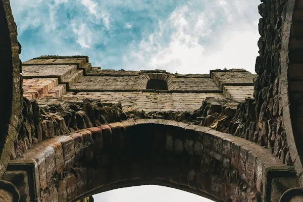 Weathered medieval stone ruin with an arch against a cloudy sky, similar to the remains at King John's Palace near Clipstone