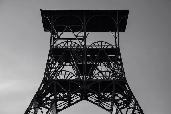Black and white silhouette of a steel pit headframe against a pale sky, the type of structure that stands over Clipstone
