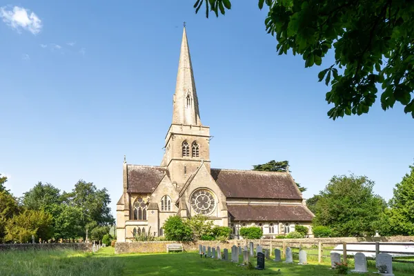 Stone parish church with a tall spire and clay tiled roofs behind a churchyard on a sunny day, similar in character to St Mary's at Edwinstowe