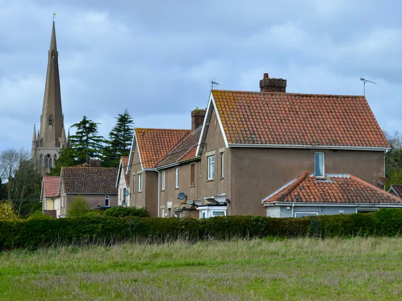 English village houses with clay tiled roofs and chimneys, with a church spire rising behind them, much like the view across older Edwinstowe