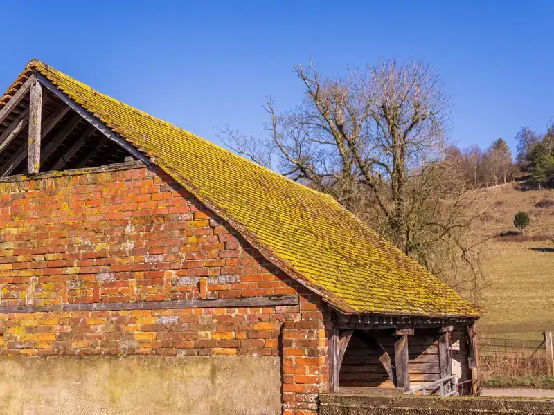 Old brick barn with a moss-covered clay tile roof and timber-framed open bay, the kind of farm building found in Old Kirkby