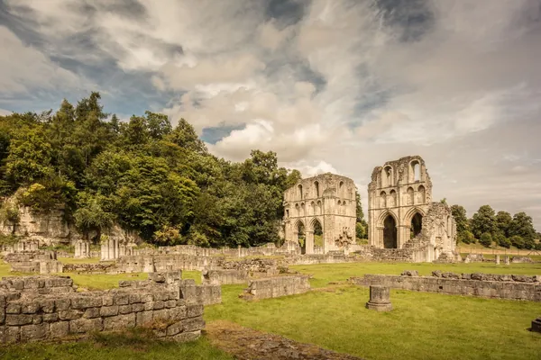 Ruined medieval abbey walls and arches on open grass under a cloudy sky in England, similar to the abbey remains at Rufford near Ollerton