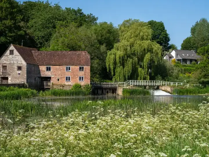 Old stone and brick mill building beside a river with a weir and willow trees, recalling the water-powered mills of Pleasley Vale