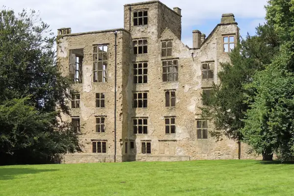 Roofless sandstone ruin of Hardwick Old Hall with tall empty window openings above a mown lawn