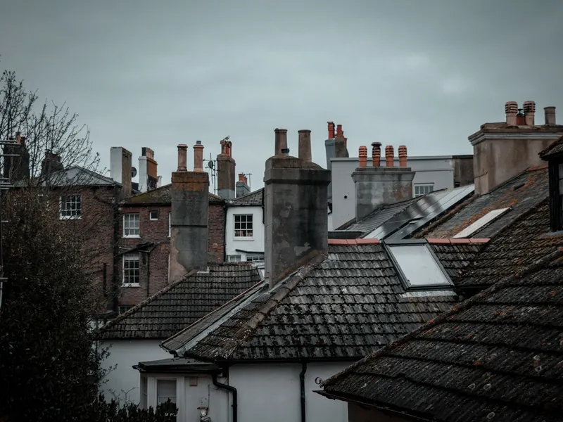 Old terraced rooftops with mossy tiles and a crowd of brick chimney stacks under a grey sky, like the backs of Sutton-in-Ashfield terraces